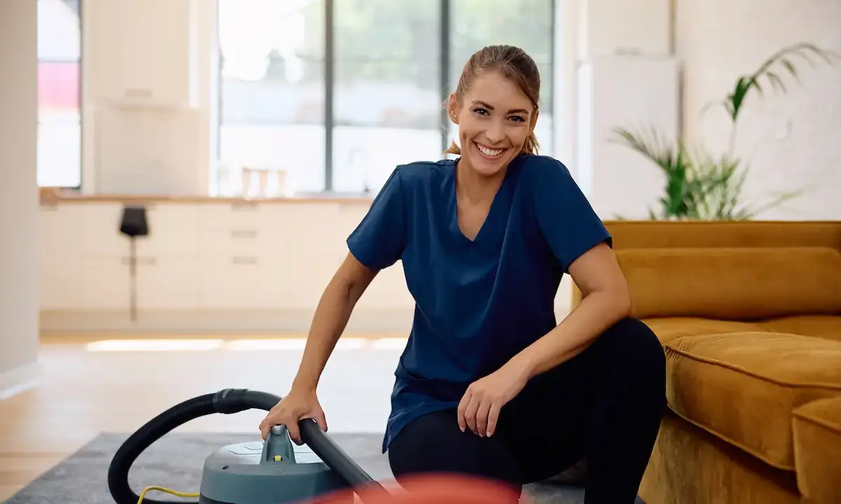 Smiling cleaner kneeling with vacuum, illustrating Opura Services spring cleaning