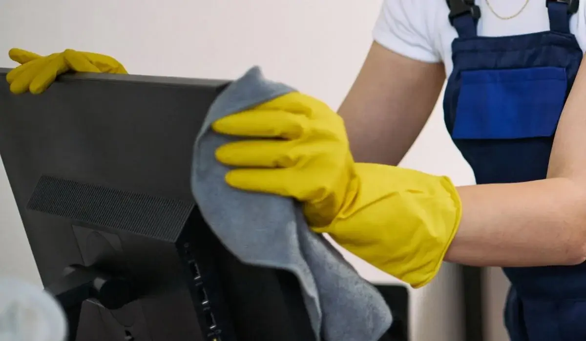 Professional cleaner with yellow gloves wiping a computer monitor