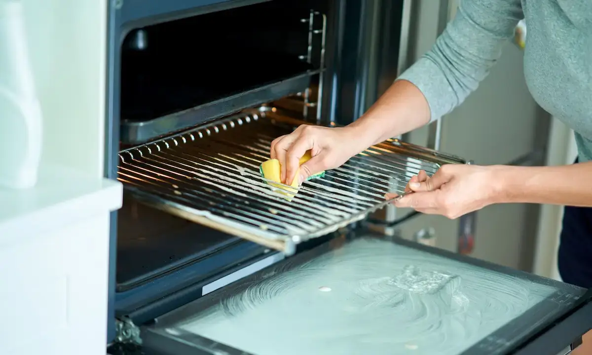 Person scrubbing oven rack and door with sponge during kitchen cleaning