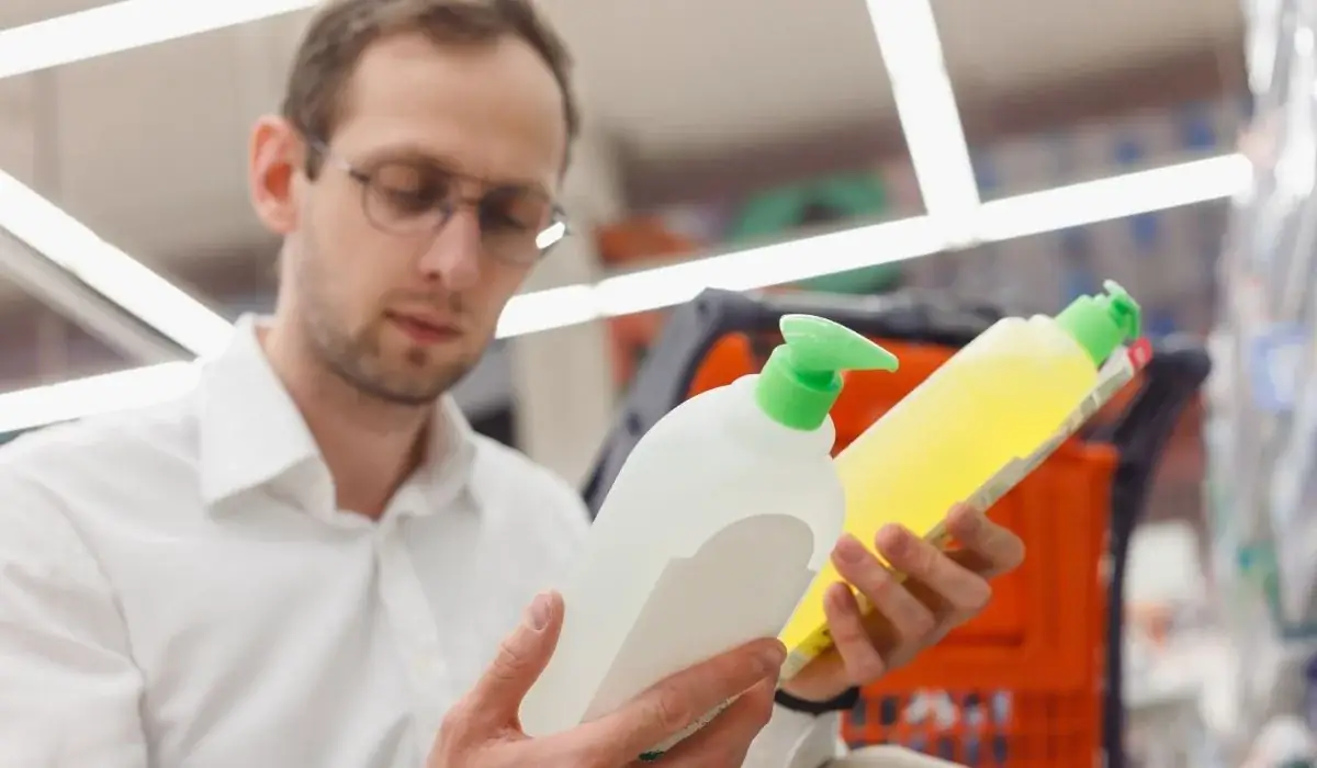 Man reading labels while comparing cleaning bottles, choosing lower-risk products